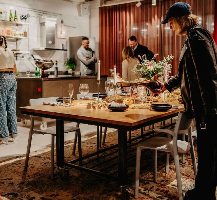 A woman pours wine at a set table.